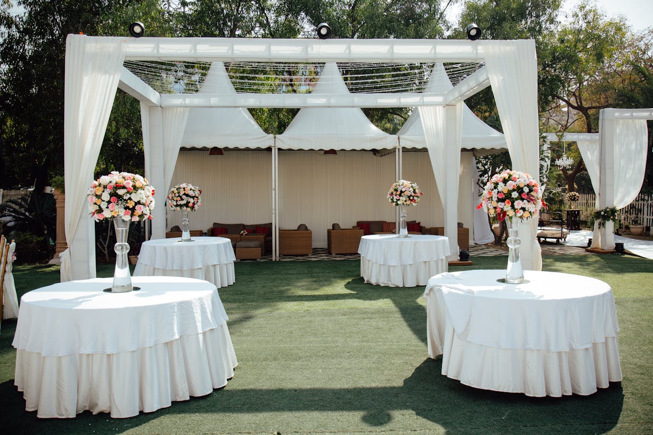 home-hero Charming outdoor wedding setup with white draped pergolas and floral centerpieces under a sunny sky.